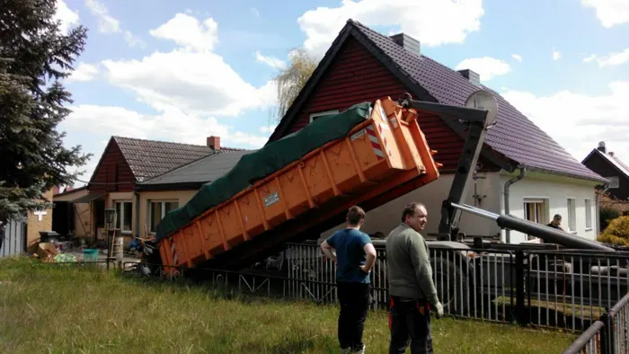 Zwei Mitarbeiter des Speicher bei einer Beräumung, ein Container wird vor einem Haus abgesetzt